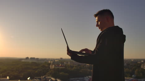Programmer-a-hacker-is-on-the-roof-with-a-laptop-at-sunset-says-error-code-on-the-keyboard-and-looking-at-the-city-view.